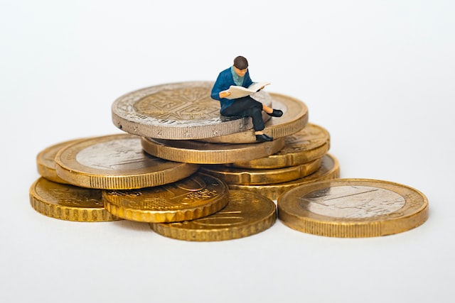 Miniatur-Figur sitzt lesend auf Euro-Münzen