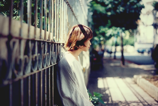 Junge Frau lehnt sich gendankenverloren an einen Zaun an