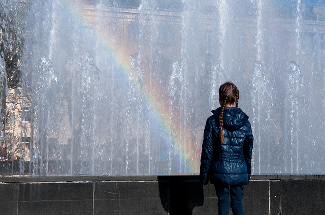 Mädchen steht vor Brunnen in dem sich ein Regenbogen bildet