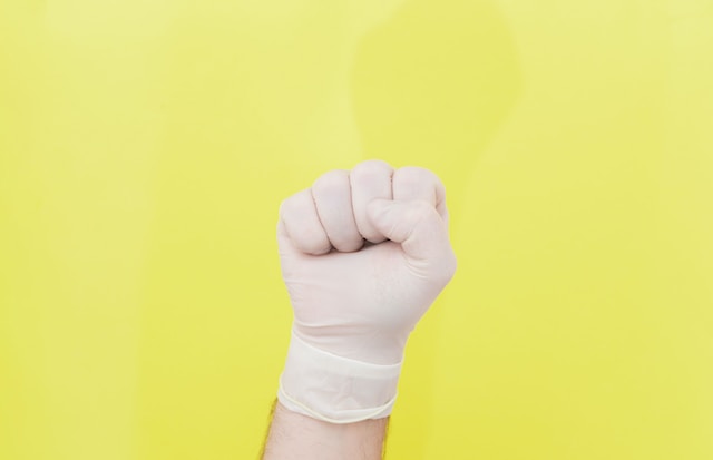 Hand im Einmalhandschuh vor gelbem Hintergrund