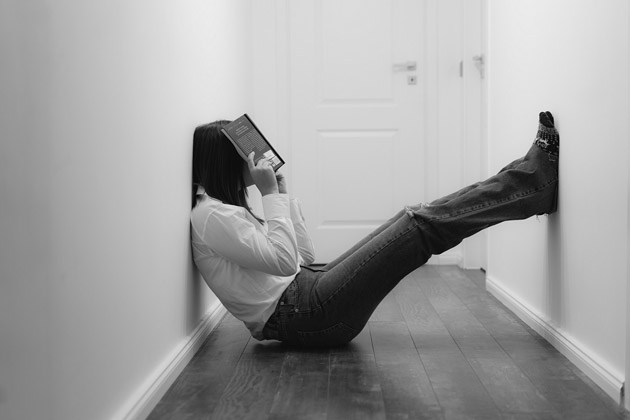 Person sitzt mit Kopf im Buch auf Boden eines Flurs 