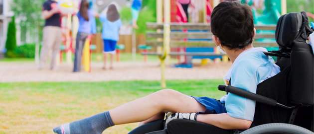 Junge im Rollstuhl schaut auf spielende Kinder im Hintergrund. 