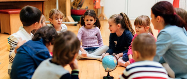 Diskutierende Kinder im Kreis mit ihrer Lehrerin und einer Weltkugel in der Mitte